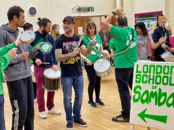 Samba drumming group being led by Mestre with drums in hands and playing instruments