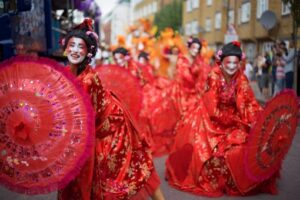 LSS Notting Hill Carnival 2016 - featured - ladies in bright red geisha costumes with umbrellas - Copyright Tristan Daws