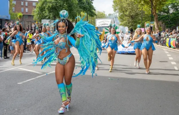 Notting Hill Carnival Parade - Samba Dancer in light blue feather wings dancing towards the camera with her troup behind her - Copyright Brian Guttridge