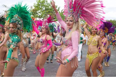 Samba dancers dancing in street for the Schools Carnival 2022, all are wearing bright coloured samba costumes and smiling