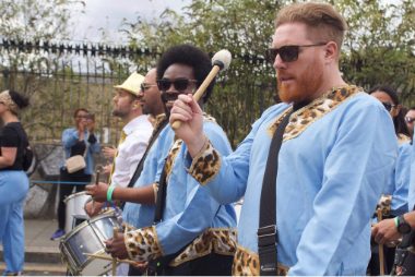 Carnival 2022 - Bateria drummers marching with drums, they wear blue tunics with some recycled leopard print from previous carnivals